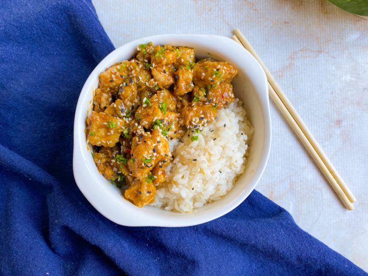 Frango ao molho de laranja à moda chinesa pronto para consumo em um prato com arroz.