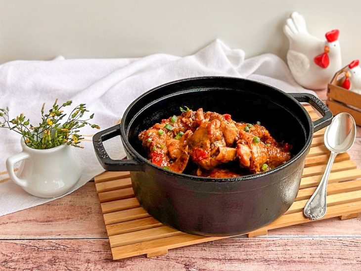 Frango ao molho simples pronto para consumo em uma panela preta sobre uma tábua.