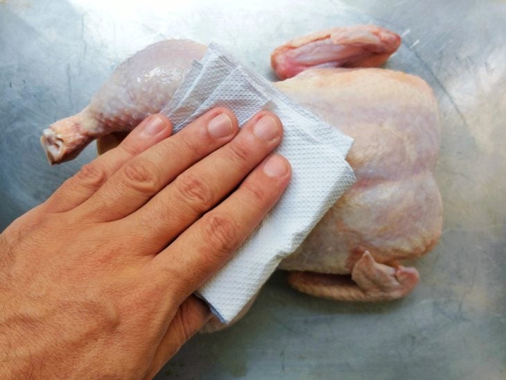 Mão segurando papel-toalha secando o frango inteiro.