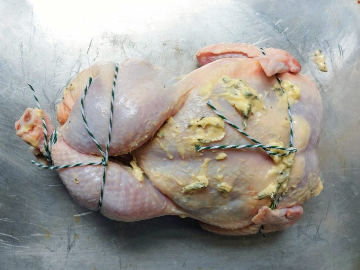 Frango inteiro com assas e coxas amarradas junto ao corpo do frango.