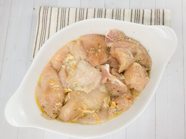 Uma forma contendo filés de frango com sal, pimenta-do-reino, mix de temperos e alho amassado.