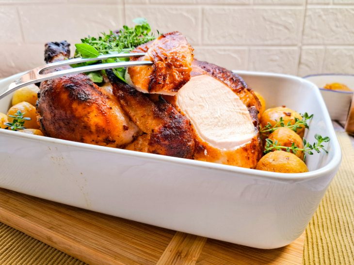 Porção de frango assado sendo retirada com um garfo de churrasco.