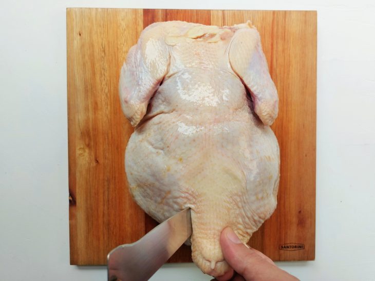 Um frango cru sendo cortado sobre uma tábua.