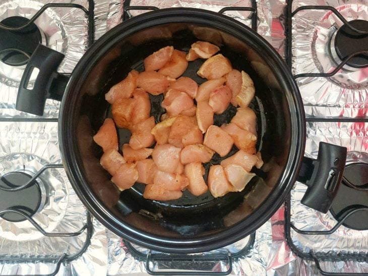 Uma panela com manteiga, óleo e pedaços de frango.