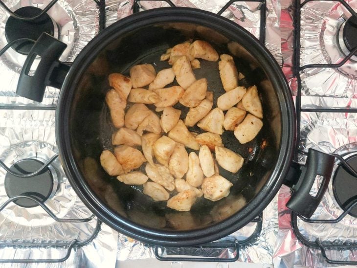 Uma panela com pedaços de frango temperados com sal, páprica, pimenta-do-reino.