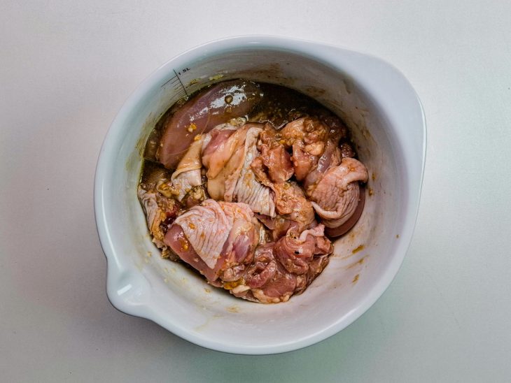 Numa tigela, o pedaços do frango marinando junto aos temperos.