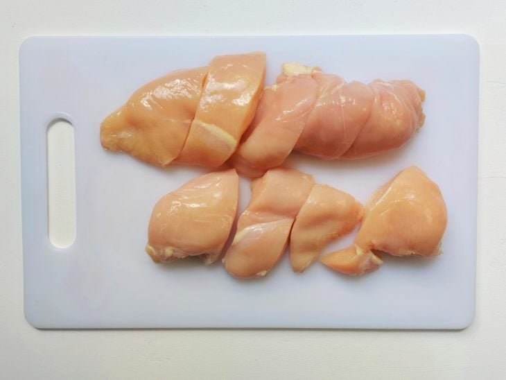 Uma tábua contendo peito de frango cortado em pedaços.