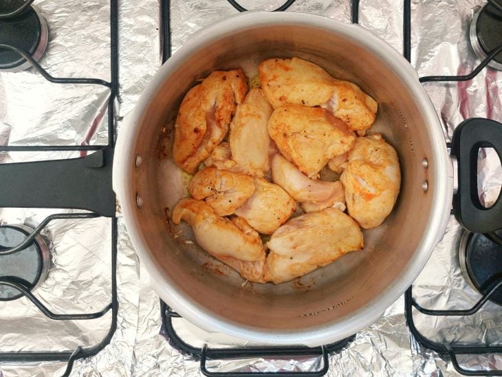 Uma panela de pressão selando os pedaços de frango.