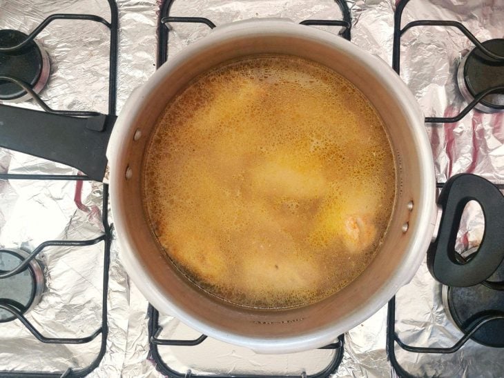 Uma panela de pressão contendo pedaços de frango e água.