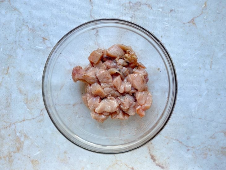 Filés de frango cortados em cubos temperados com limão, sal, pimenta-de-reino e páprica picante em uma tigela de vidro.