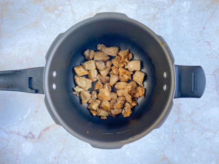 Cubos de frango grelhados em uma panela de pressão com azeite.