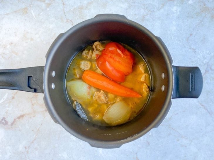 Cebola, dentes de alho, cenoura, tomate e folhas de louro na panela de pressão com água.