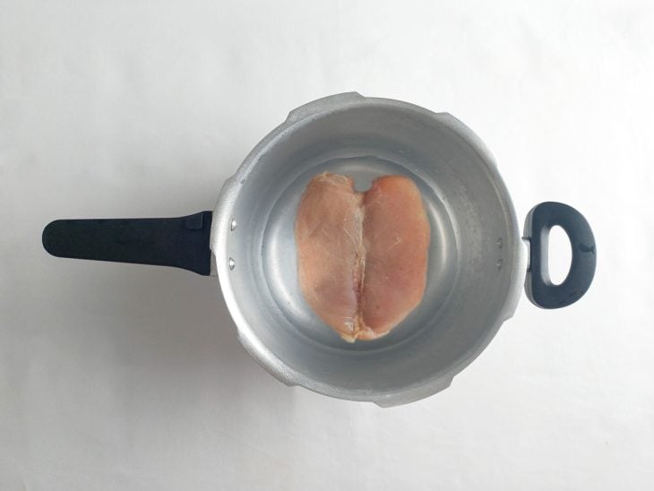 Frango colocado em uma panela de pressão com água.