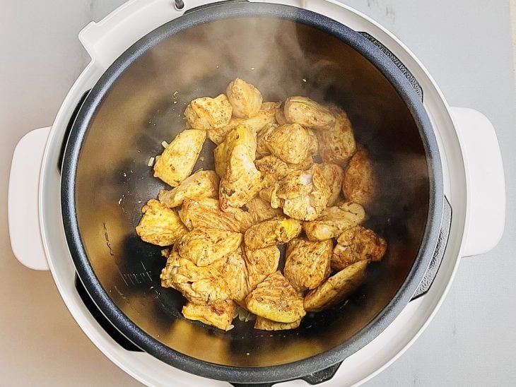 Cebola e frango refogando dentro da panela elétrica.