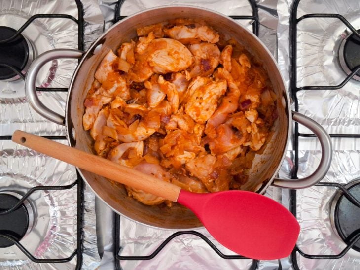 Pedaços de frango e temperos adicionados na panela.