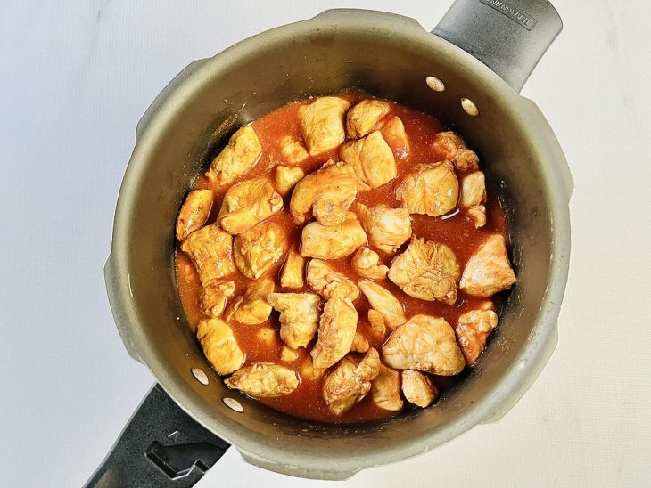 Água e passata de tomate adicionadas na panela com o frango.