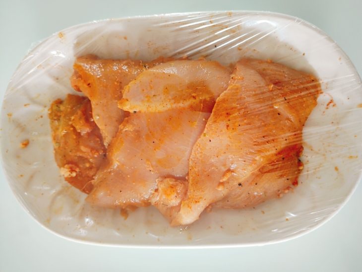Filés de frango temperados em uma tigela coberta com plástico filme para marinar.