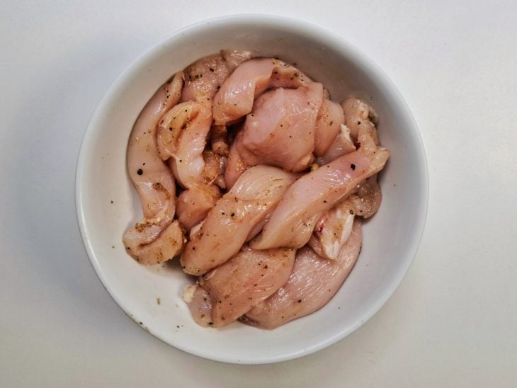 Frango temperado com sal, páprica e pimenta-do-reino dentro de uma tigela.