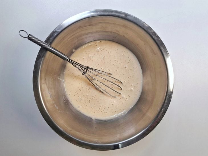 Farinha de trigo, ovos, amido de milho, água, fermento, páprica, sal, pimenta-do-reino e cebola em pó misturados em uma tigela de alumínio.