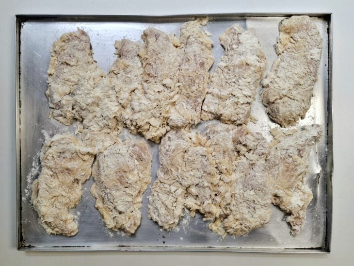 Tiras de frango empanadas em uma forma de alumínio.