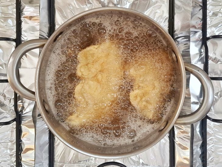 Tiras de frango fritando em uma panela com óleo.