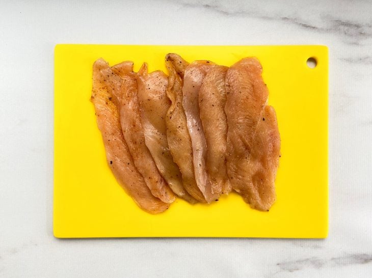 Uma tábua contendo filés de frango temperados.