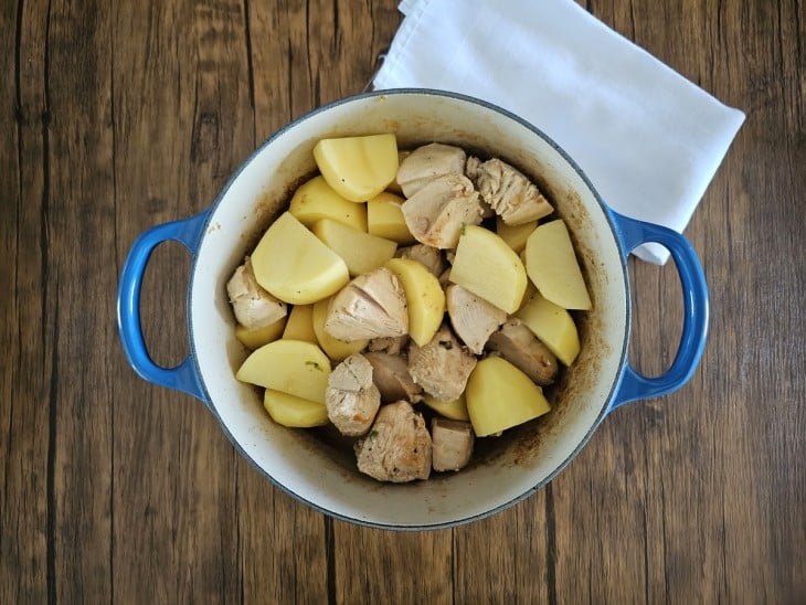 Uma panela contendo pedaços de frango com pedaços de batatas.