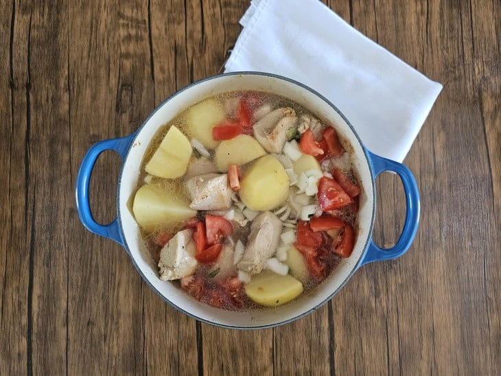 Uma panela contendo pedaços de frango, pedaços de batatas, tomates e água.