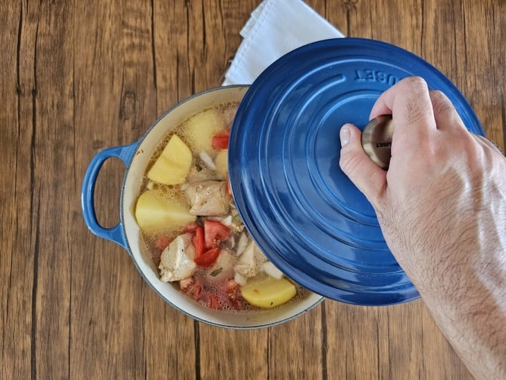 Uma panela contendo pedaços de frango, pedaços de batatas, tomates e água.