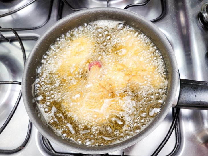 Panela com coxinhas fritando em óleo quente, borbulhando um pouco.