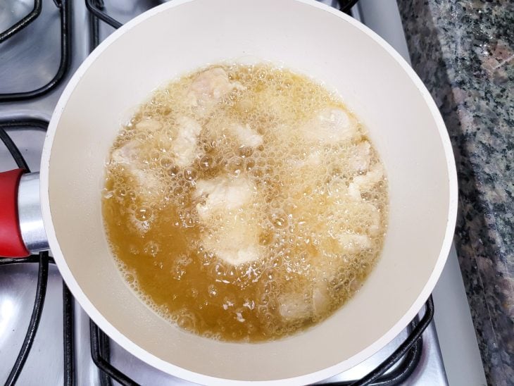 Panela com frango sendo frito no óleo.