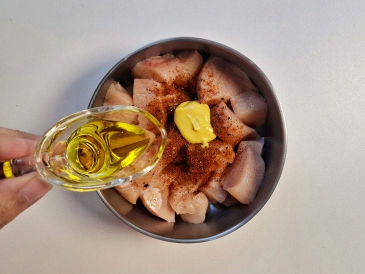 Cubos de frango em uma tigela redonda com temperos e azeite em outro recipiente para ser adicionado.