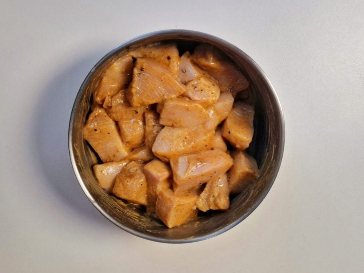 Cubos de frango envolvidos nos temperos adicionados na tigela redonda.