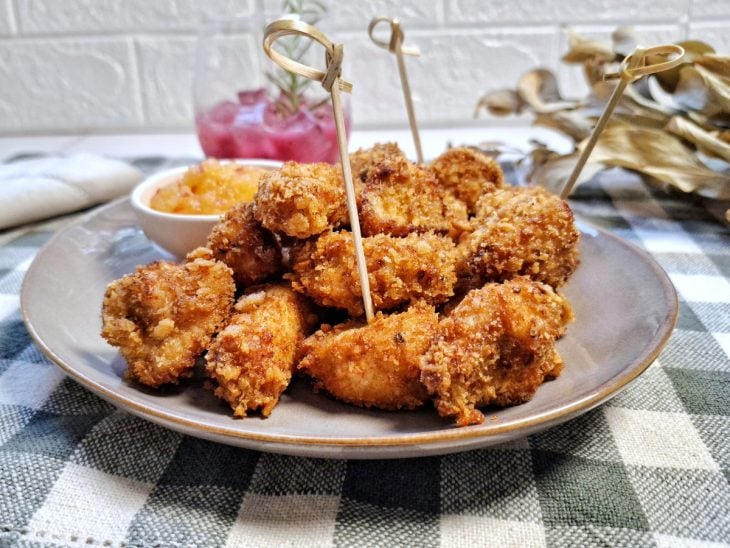 Frangos fritos servidos em um prato redondo cinza acompanhados por molho e palitos para espetar.