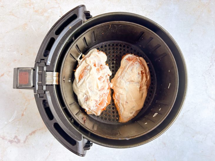Frango acomodado no cesto da air fryer com a cobertura cremosa.