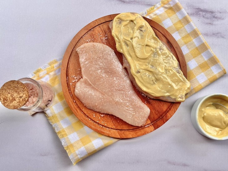 Um filé de frango temperado e outro com mostarda por cima.