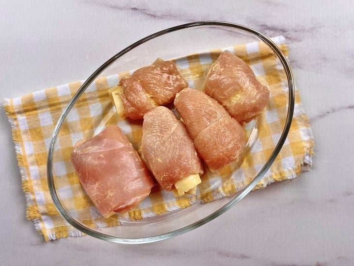 Filés de frango enrolados e recheado com mussarela dentro de um refratário.