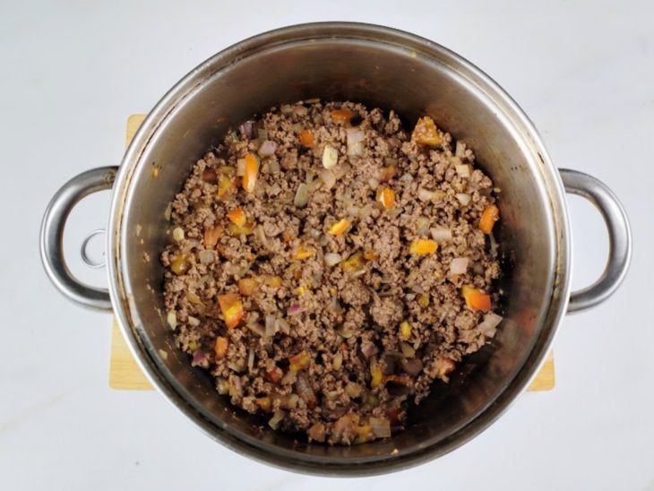 Uma panela com carne moída, alho, cebola, tomate e temperos.