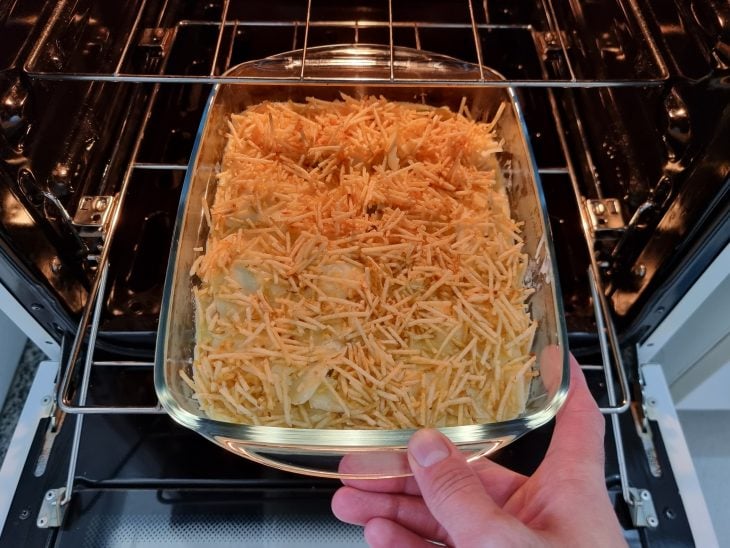 Refratário com fricassê de frango salpicado com batata palha sendo colocado no forno.