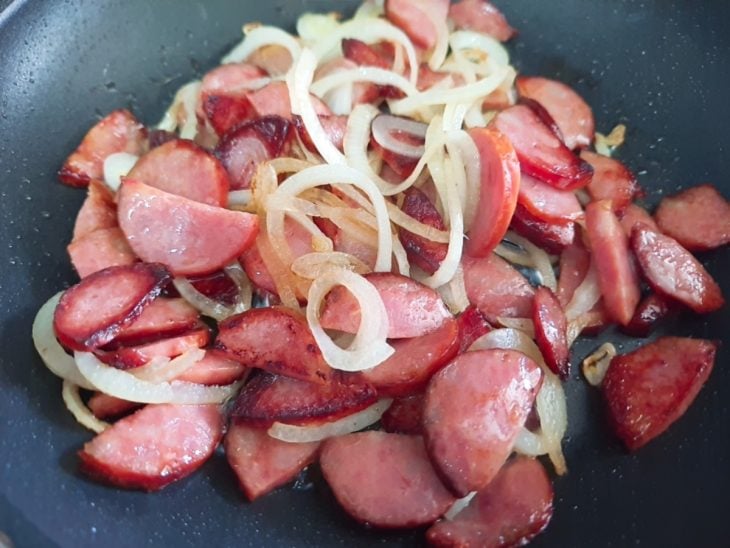 Uma frigideira com a calabresa e cebola a dourarem.
