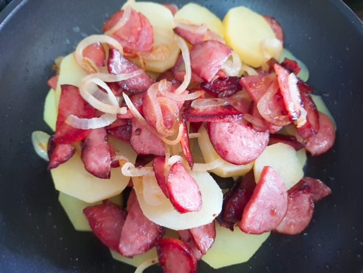Uma frigideira com calabresa, batata e cebola.