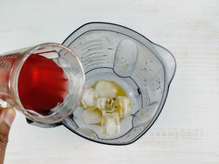 Chá, rum branco, licor de maracujá, suco de limão, açúcar e gelo em um liquidificador.