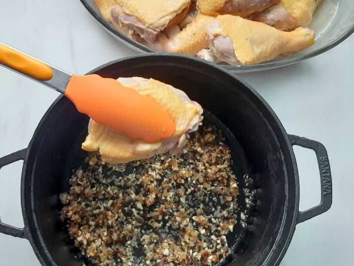 Uma panela com alho, cebola e pedaços de frango.