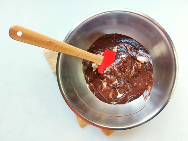 Chocolate e creme de leite sendo misturados com o auxílio de uma espátula.
