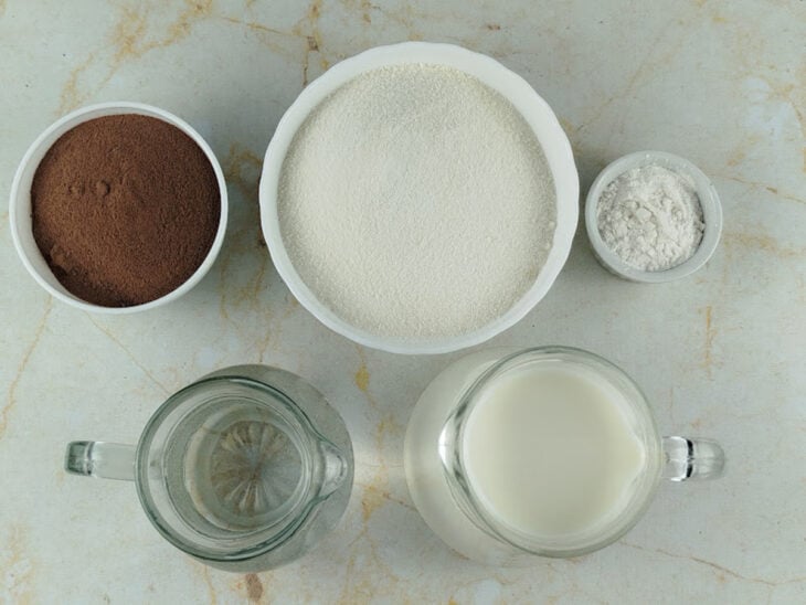 Ingredientes organizados na bancada com leite, água, açúcar, liga neutra e achocolatado separados para o preparo.