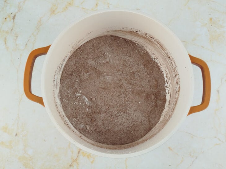 Ingredientes secos sendo misturados em uma panela até ficarem homogêneos.