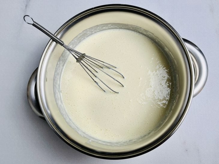 Leite condensado, creme de leite e leite em pó misturados em uma panela.