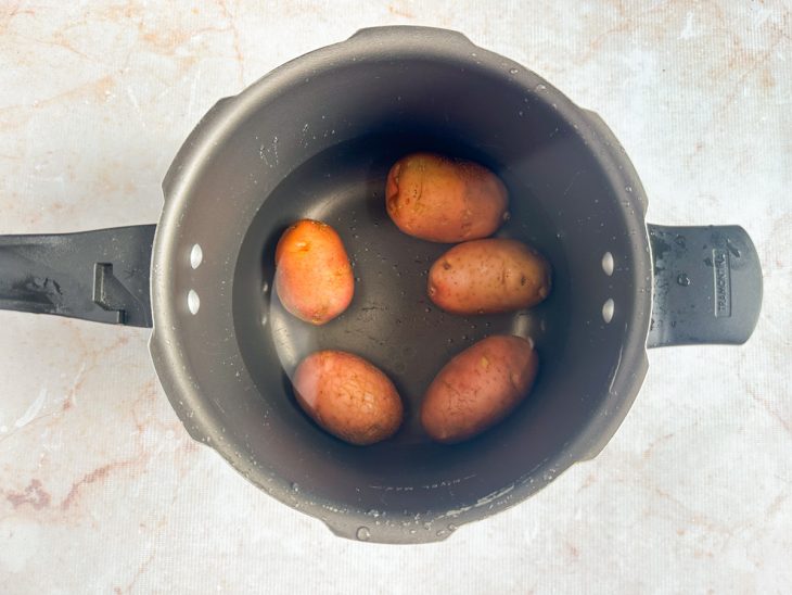 Batatas cozinhando inteiras em panela com água e sal.