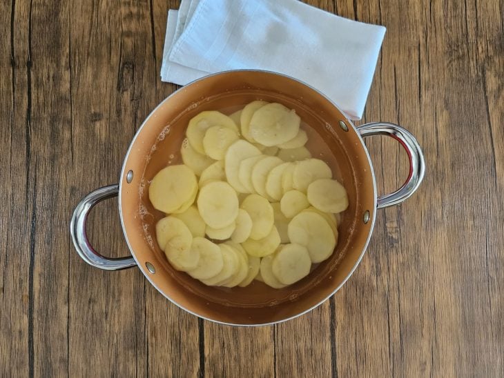 Uma panela contendo rodelas de batatas sendo cozidas.