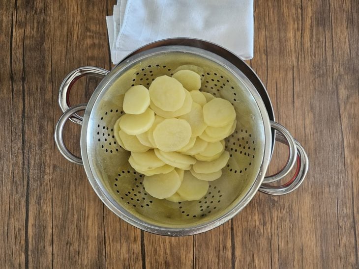 Uma panela espagueteira com rodelas de batatas cozidas.